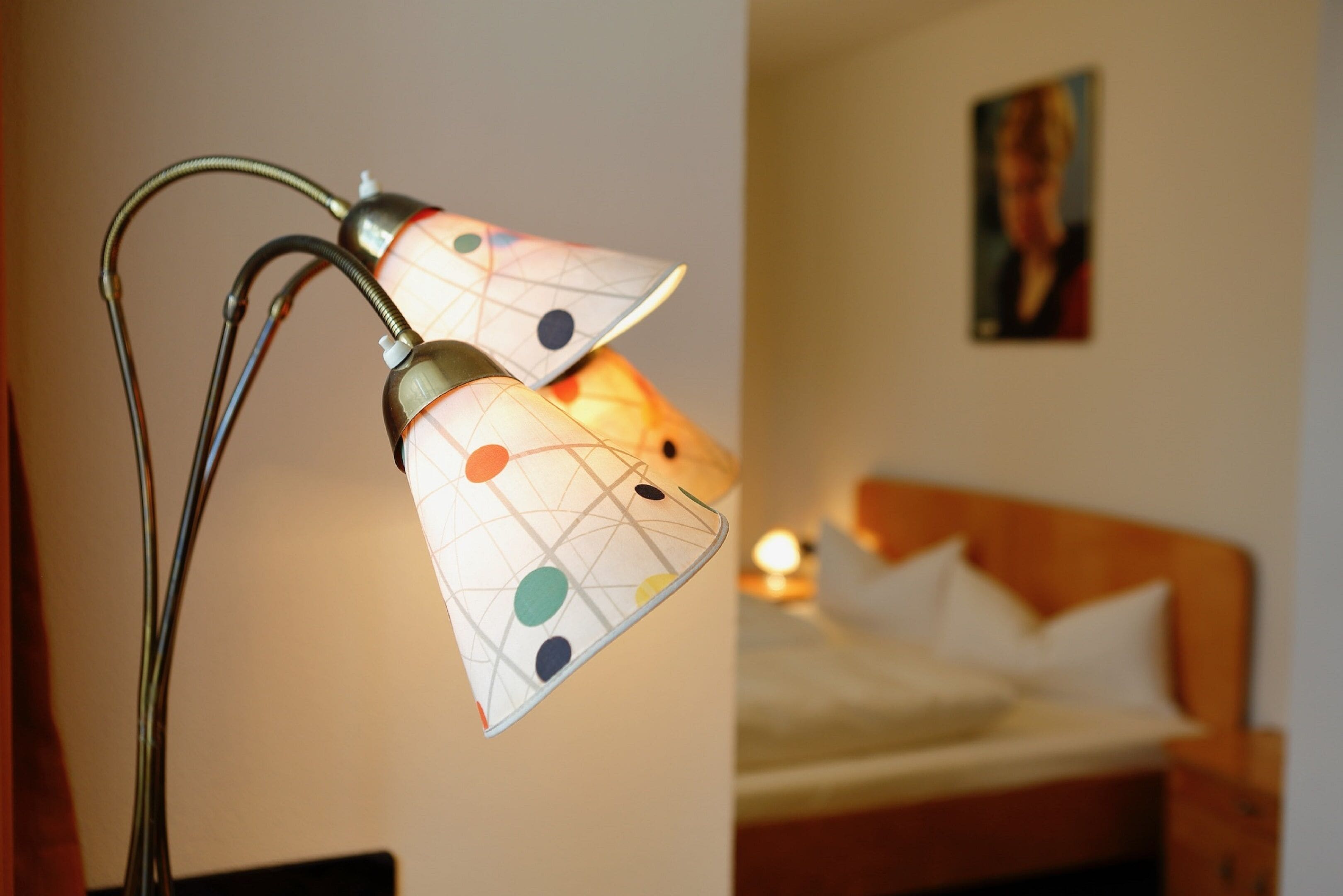 A lamp with a geometric pattern on its lampshade, a bed with white bedding, and a painting on the wall.