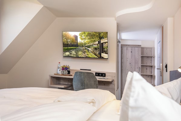 A modern hotel room with a bed, a desk, and a TV mounted on the wall displaying a scenic view.