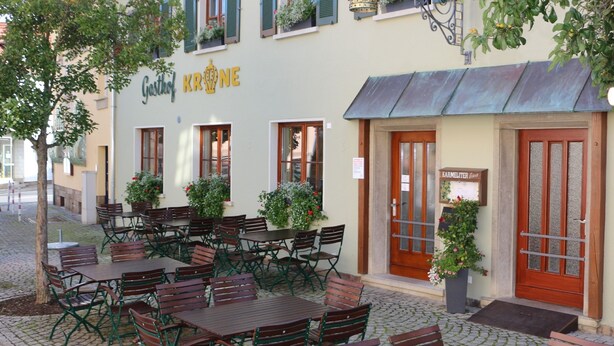 Un restaurante con terraza, un letrero que dice "Gasthof KRONE" y un letrero de "KARLSTEINER" cerca de la entrada.