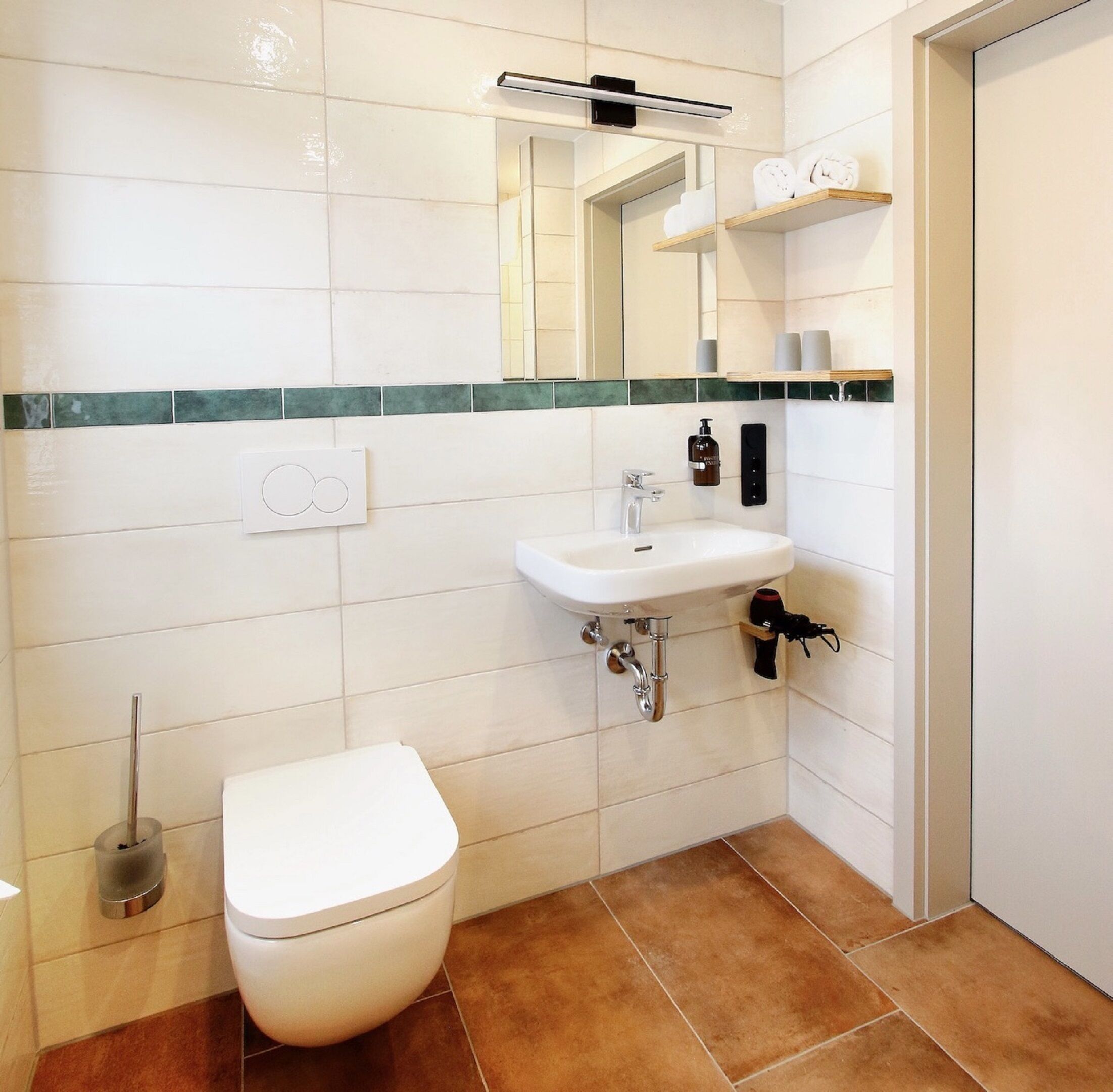 Un baño con inodoro, lavabo y espejo. Hay toallas y artículos de aseo en un estante.