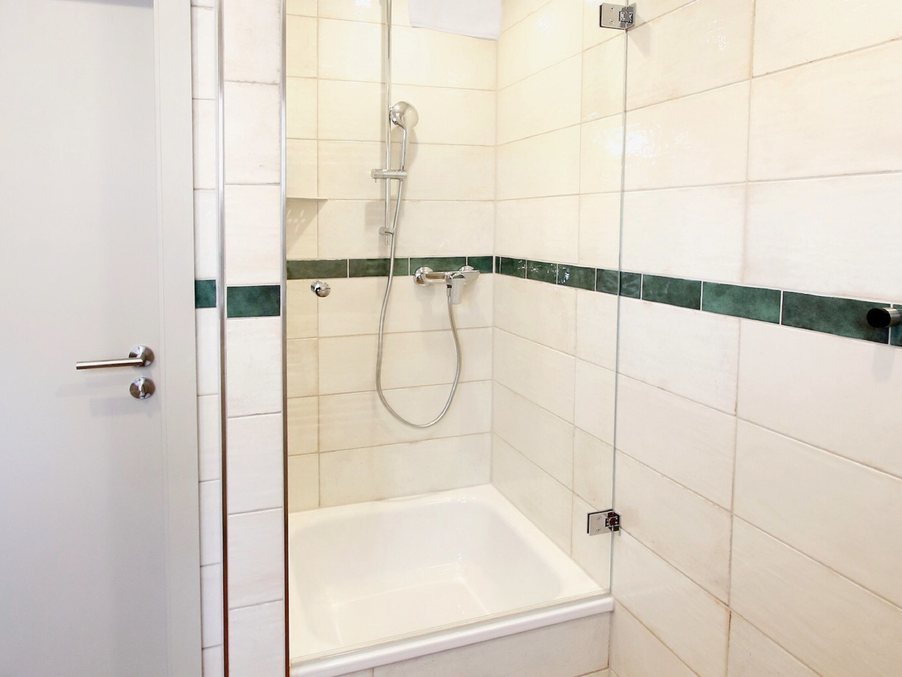 A small, enclosed shower area with a glass door, a showerhead, and a white bathtub.