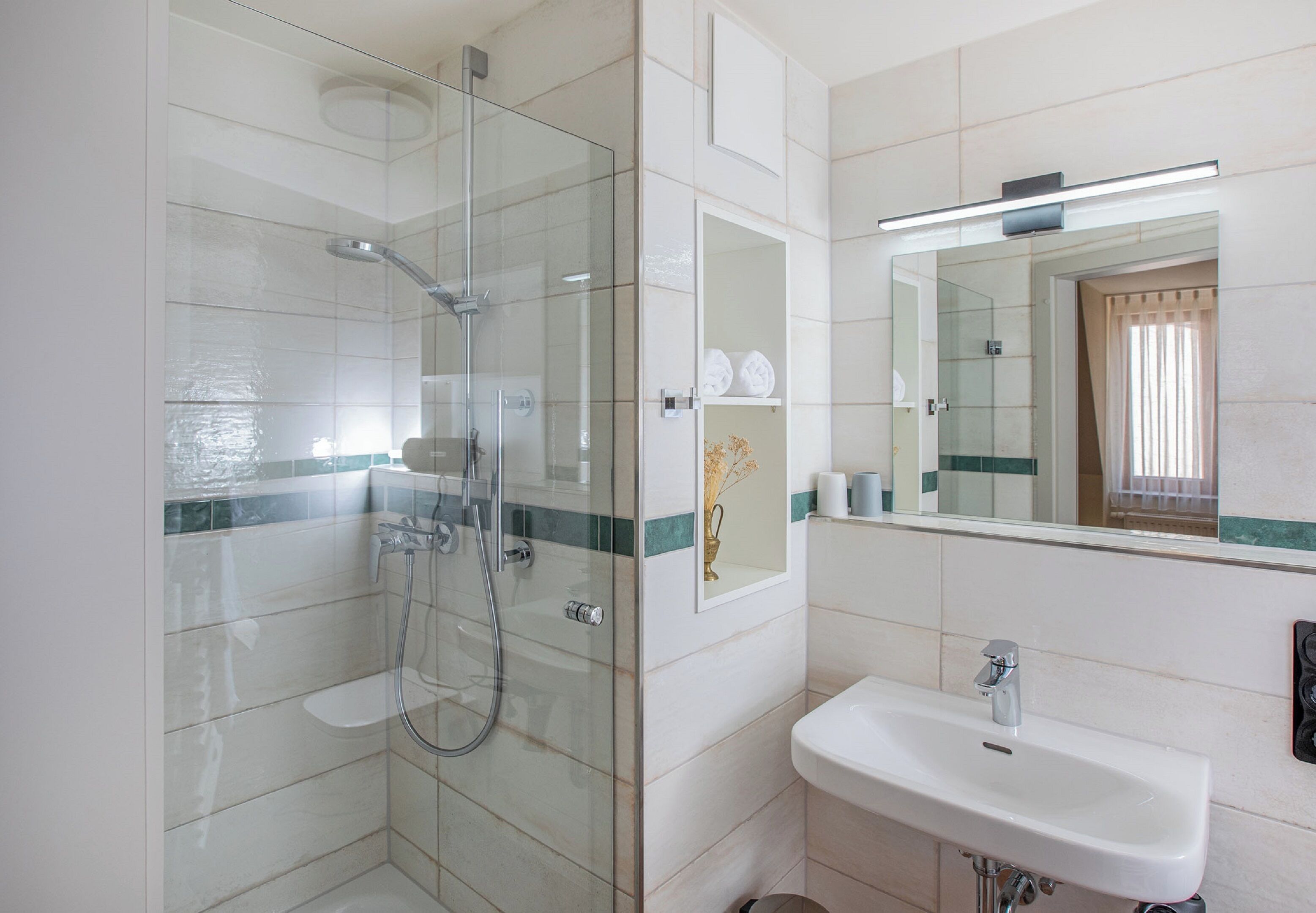 Un baño moderno con ducha de vidrio, lavabo blanco y espejo sobre él.
