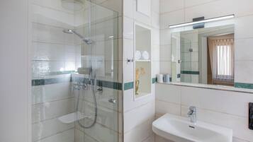 Un baño moderno con ducha de vidrio, lavabo blanco y espejo sobre él.