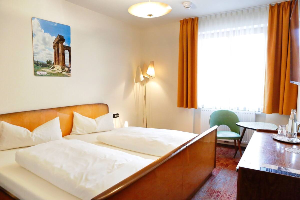 Hotelkamer met een bed, een bureau, een stoel, een lamp en een schilderij van oude ruïnes.