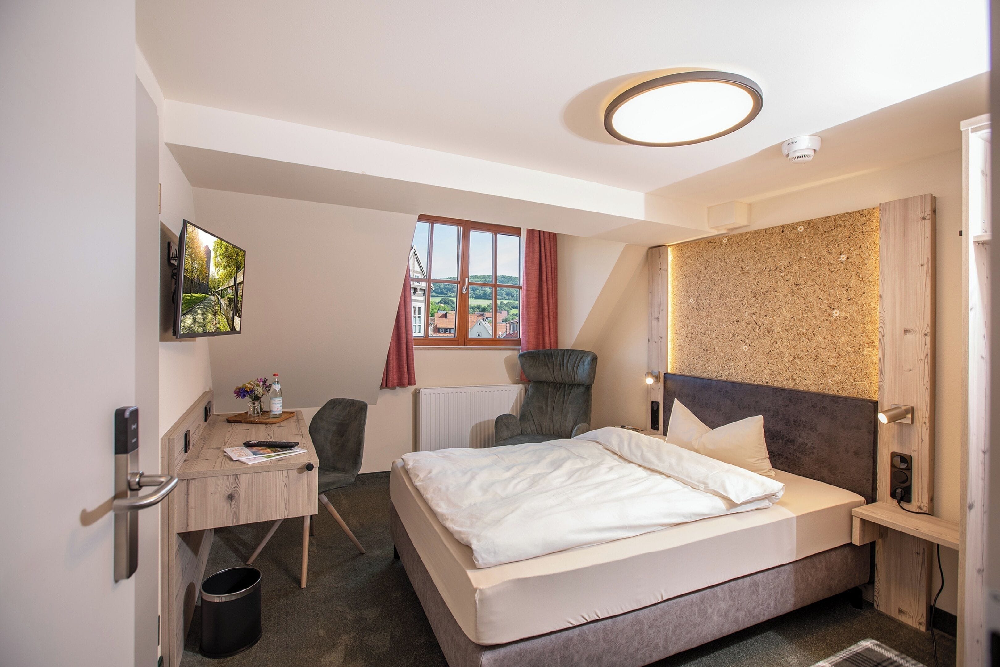 Una habitación de hotel moderna con cama, escritorio, silla y vista a un edificio a través de una ventana.
