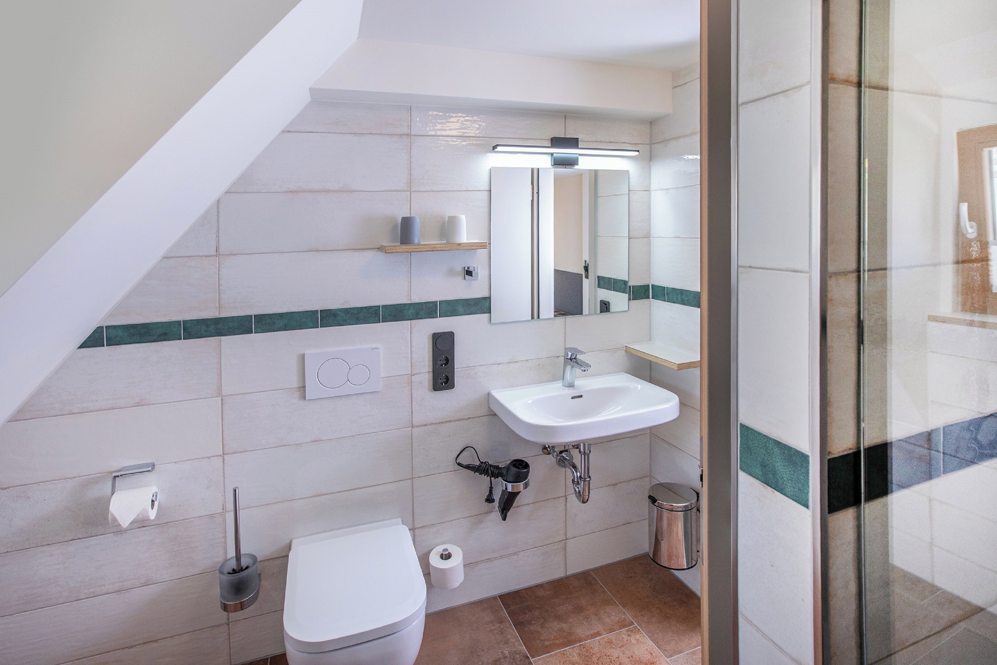 Un bagno moderno con un water bianco, un lavandino, uno specchio e una zona doccia.