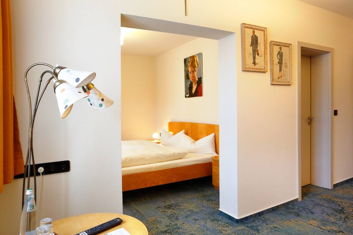 Een hotelkamer met een bed, nachtkastje, lamp en een schilderij aan de muur.