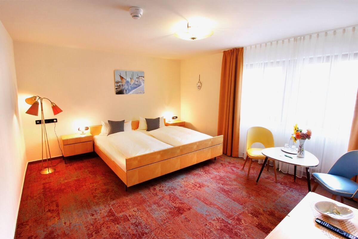 Hotelkamer met een bed, nachtkastjes, een bureau met stoel, een lamp, een schilderij aan de muur en een raam met gordijnen.