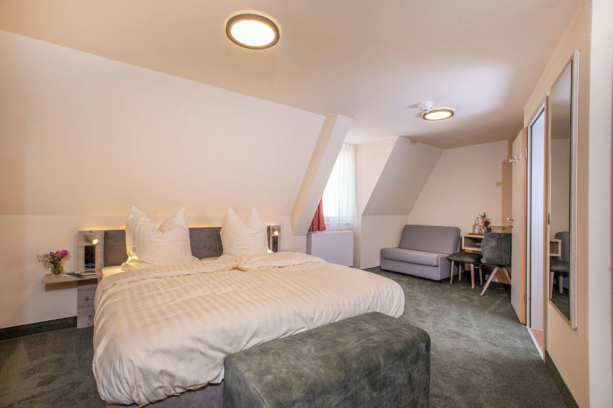 Een slaapkamer met een groot bed, een bureau, een stoel en een tafeltje met een bloevas.