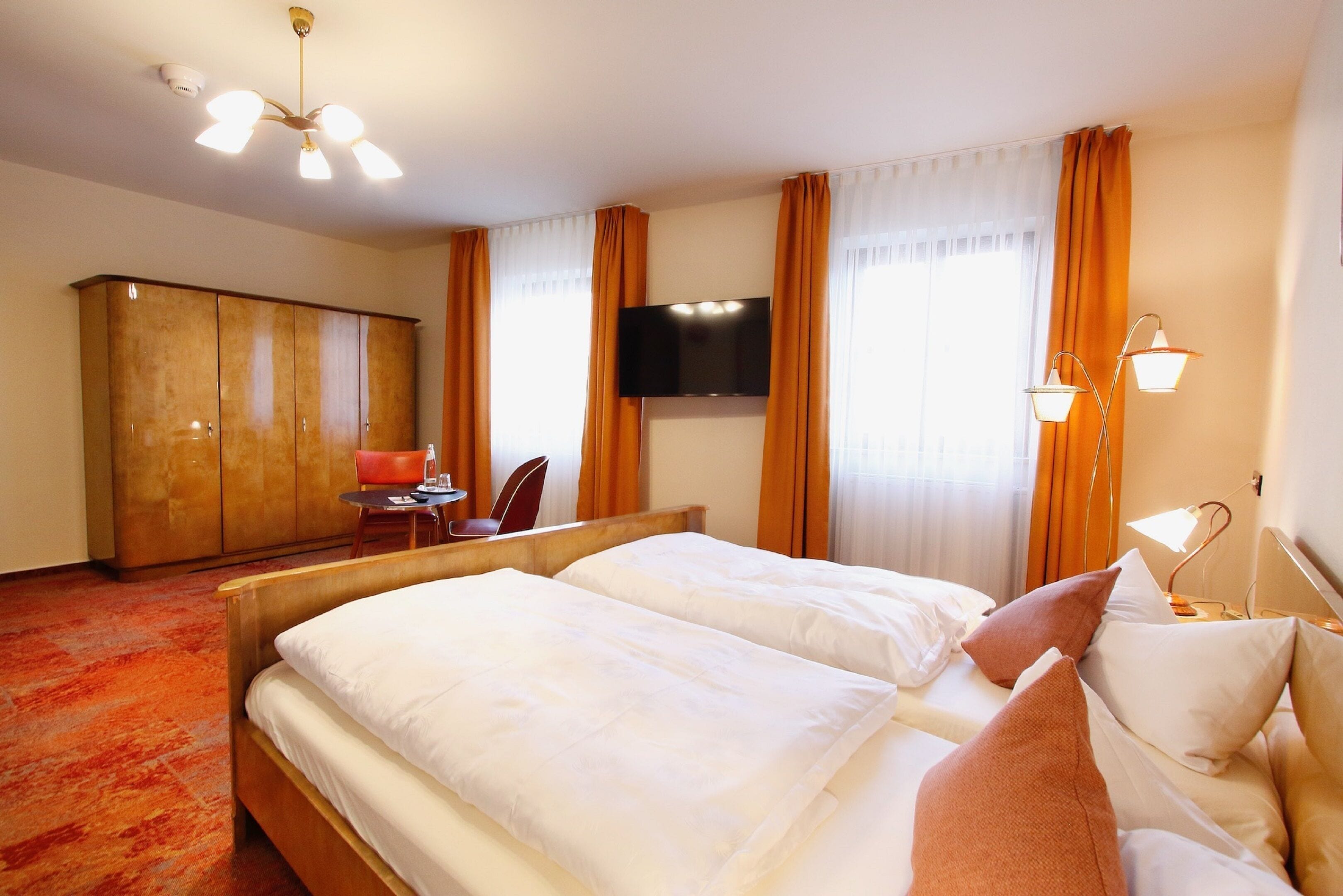 A hotel room with a bed, a desk, a chair, a wardrobe, a TV, and a window with curtains.