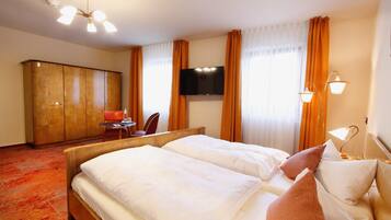 A hotel room with a bed, a desk, a chair, a wardrobe, a TV, and a window with curtains.