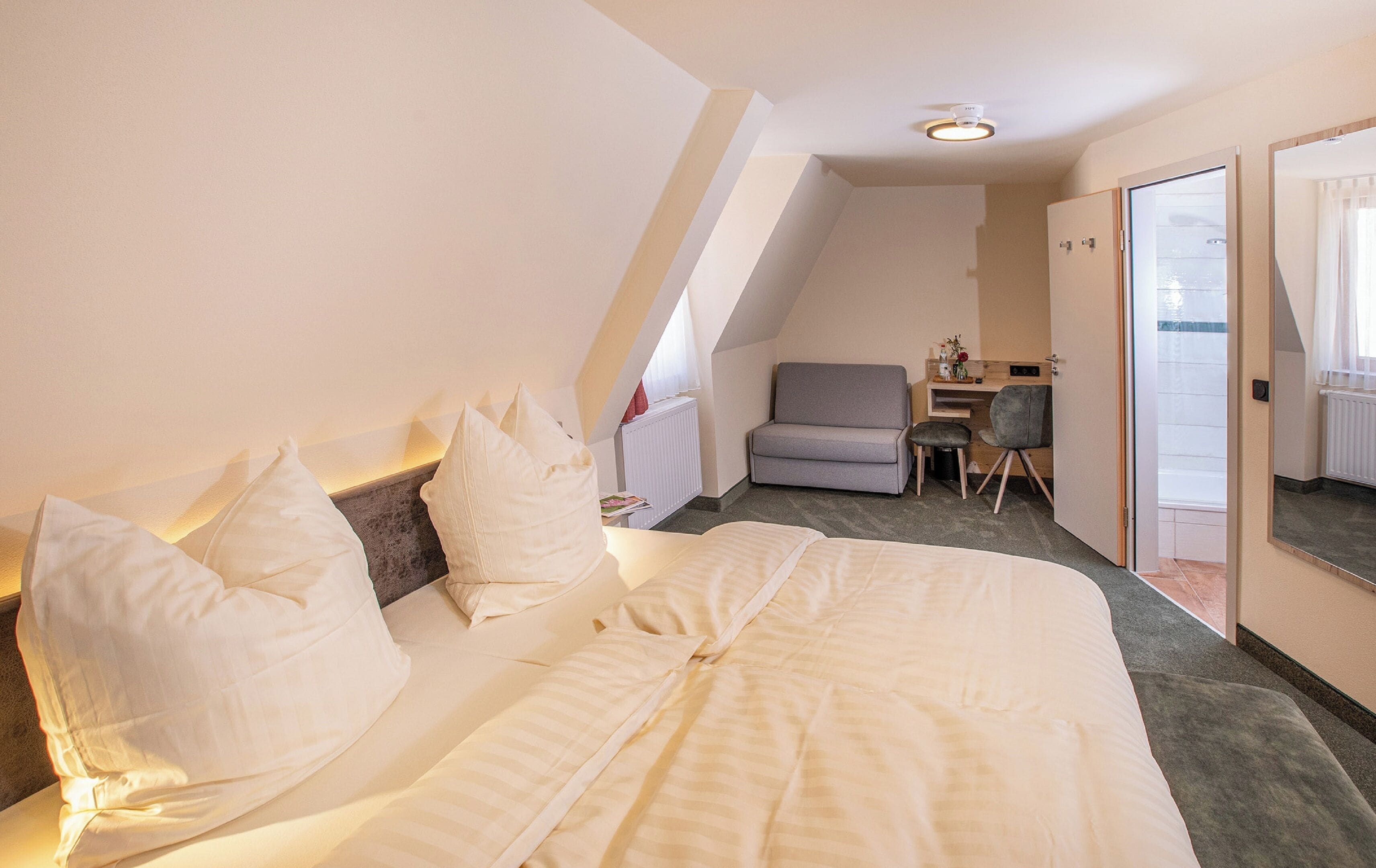 A bedroom with a large bed, a desk, and a chair, with a view of the outside through a door.