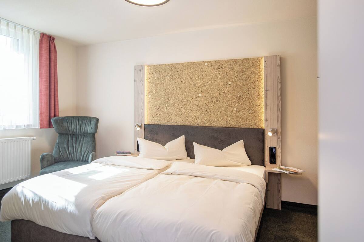 Hotelkamer met een groot bed, een stoel, een hoofdbord met een gestructureerd paneel en een nachtkastje met een lamp.