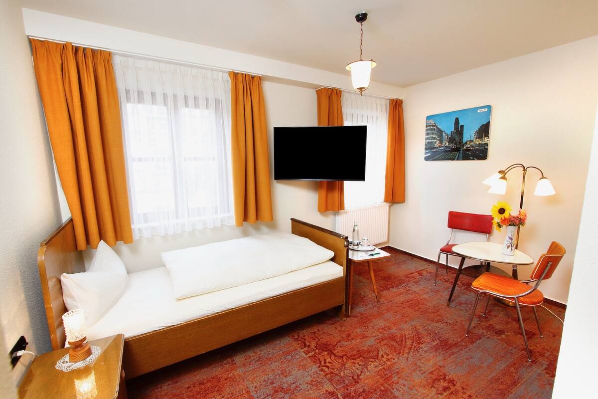 Een hotelkamer met een bed, een televisie, een klein tafeltje met een stoel, en een raam met gordijnen.