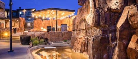 A rock formation with a pool, outdoor seating, and a building with string lights.