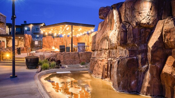 A pool area with a hot tub, surrounded by rock formations and a building with outdoor seating. - Sage Creek at Moab Tunnel Arch Hideaway (Moab)