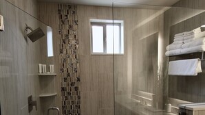 A modern shower area with a glass door, a patterned tile wall, and a built-in shelf with toiletries. - Sage Creek at Moab Tunnel Arch Hideaway (Moab)
