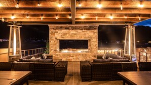 An outdoor patio with a stone fireplace, wicker furniture, and string lights. - Sage Creek at Moab Tunnel Arch Hideaway (Moab)