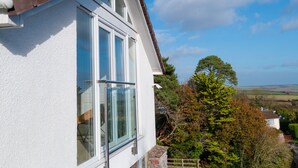 A white building with large windows and a brown roof, surrounded by trees and a clear sky. - Ultimate Coastal Escape | Stylish  | Estuary Views (Salcombe)