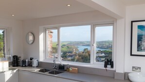 A modern kitchen with a large window overlooking a scenic landscape. - Ultimate Coastal Escape | Stylish  | Estuary Views (Salcombe)