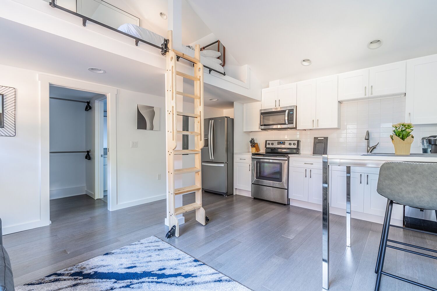 Una cocina moderna con armarios blancos, electrodomésticos de acero inoxidable y una escalera de madera.