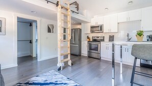 Una cocina moderna con armarios blancos, electrodomésticos de acero inoxidable y una escalera de madera.