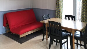 Ein Zimmer mit einem Holzespeisetisch, schwarzen Stühlen, einem roten Sofa, einem Deckenventilator und einem Fenster mit gemusterten Vorhängen.