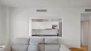 A modern living room with a sofa and a small wooden table. A kitchen is visible in the background with white cabinets and a countertop. - Panoramic Terrace w/pool by Costarentals - Ref 43 (Benalmádena)