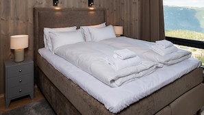 A bedroom with a large bed, two bedside lamps, a nightstand, and a view of the outdoors. - Gausta Residence (Tinn)