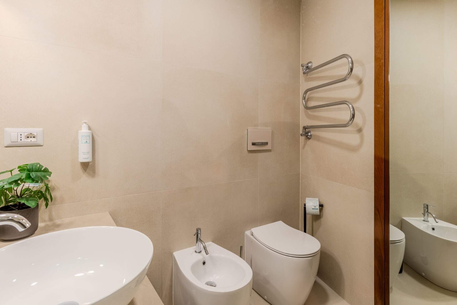 Ein modernes Badezimmer mit einem großen, ovalen Waschbecken, einem Bidet, einer Toilette und einer Dusche mit Haltegriffen.