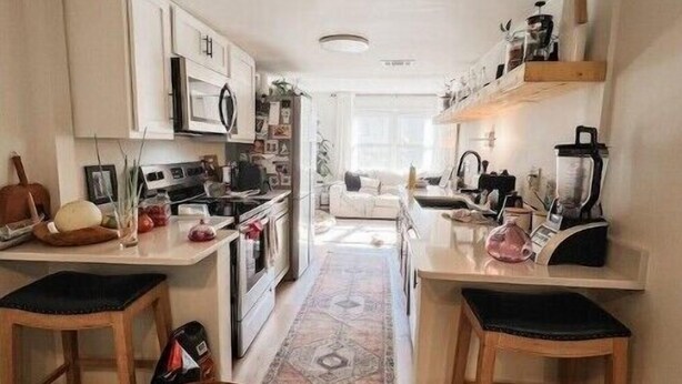 A compact kitchen with white cabinets, a central island, and bar stools.