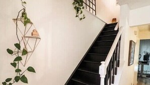 A staircase with a white railing and black steps, leading to a landing with a geometric wall decoration and a potted plant.