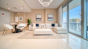 Ein modernes Wohnzimmer mit einem Ecksofa, einem Essbereich mit rundem Tisch und großen Fenstern mit Blick auf eine Baustelle.