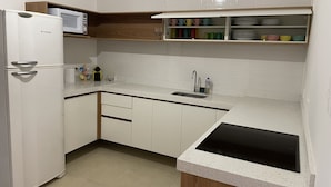 A kitchen with white cabinets, a microwave, a sink, and a countertop. - Morada City Hostel (São Paulo)