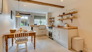A kitchen with white cabinets, a wooden dining table, and a built-in oven. - Exquisitely presented Cotswold holiday cottage - Little Cottage (Stow-on-the-Wold)