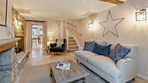 A living room with a white sofa, a coffee table, a fireplace, a stone wall, and a staircase. - Exquisitely presented Cotswold holiday cottage - Little Cottage (Stow-on-the-Wold)