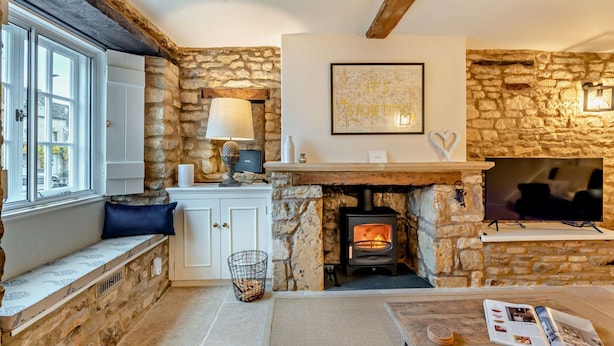 A cozy room with stone walls, a fireplace, a window with a view, and a table with a magazine. - Exquisitely presented Cotswold holiday cottage - Little Cottage (Stow-on-the-Wold)