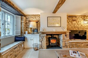 Una habitación acogedora con paredes de piedra, chimenea, ventana con vistas y una mesa con una revista.