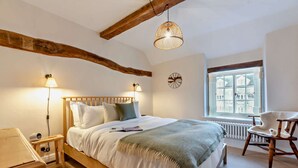 A bedroom with a wooden bed, bedside lamps, a window with a view, and a chair. - Exquisitely presented Cotswold holiday cottage - Little Cottage (Stow-on-the-Wold)