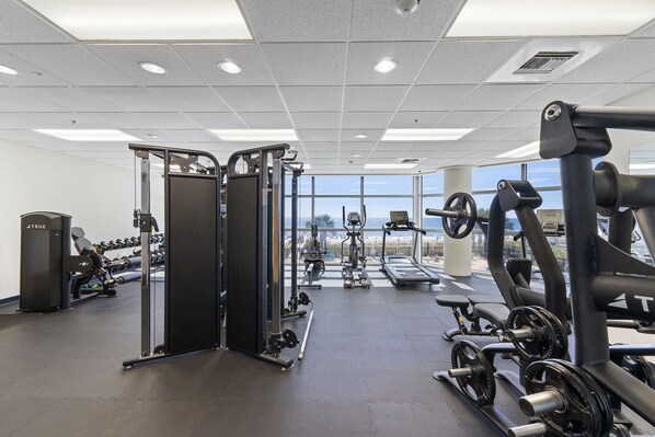 A gym with various exercise equipment, large windows, and a view of the beach.