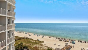A beach with a view of the ocean, a sandy beach, and a building with balconies.