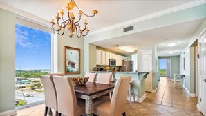 A dining area with a chandelier, a painting of a boat, and a view of the ocean.