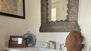 A bathroom with a white sink, dark wooden cabinets, a large mirror, and a decorative wicker basket. - Renovated Fisherman’s Cottage  (Lower Township)
