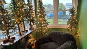 A cozy room with a plush chair, a small table with a decorative item, and three Christmas trees with lights. - Renovated Fisherman’s Cottage  (Lower Township)