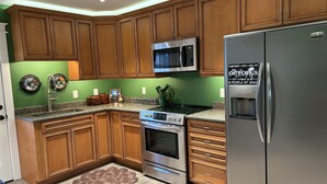 A kitchen with wooden cabinets, a stainless steel refrigerator, a microwave, and a stove. - Renovated Fisherman’s Cottage  (Lower Township)