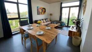 Ein modernes Wohnzimmer mit einem Holzesstisch, gedeckt für vier Personen, einem Sofa, einem Sitzsack und einem Bild an der Wand.