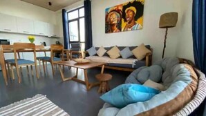 Ein modernes Wohnzimmer mit einer Couch, einem Esstisch und Stühlen. An der Wand hängt ein Gemälde und auf einem Beistelltisch steht eine Lampe.