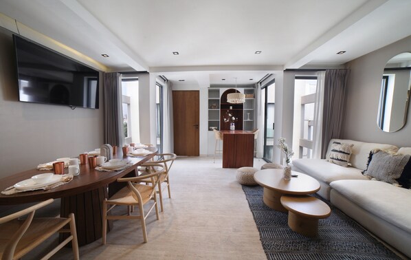 A modern living room with a dining area, a sofa, and a TV mounted on the wall.