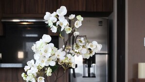 Eine transparente Glasvase mit weißen Blumen und Kieselsteinen auf einem Holztisch in einer Küche.