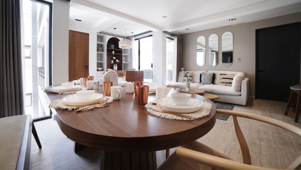 Ein modernes Wohnzimmer mit einem runden Esstisch, gedecktem Tisch für eine Mahlzeit, einer Couch und einem großen Fenster mit Vorhängen.